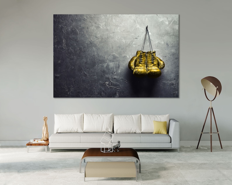 May include: A pair of gold boxing gloves hanging on a hook against a textured gray wall.