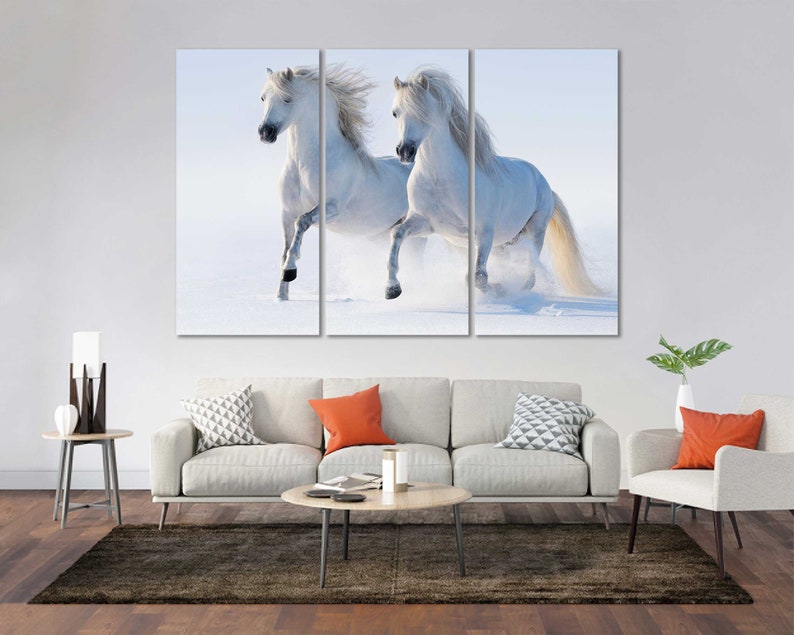 May include: Two white horses run through a snowy field, their manes flowing in the wind.