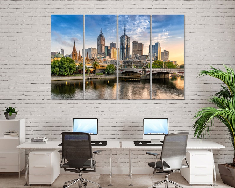May include: A panoramic view of the Melbourne skyline with a bridge in the foreground. The city is bathed in the warm glow of sunrise, with the buildings reflecting the light. The river is calm and still, with a few boats visible in the distance.