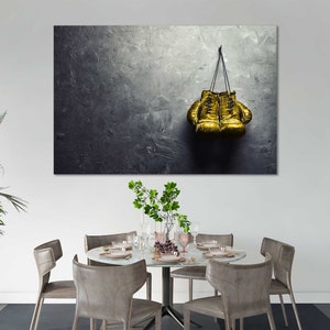 May include: A pair of gold boxing gloves hanging on a hook against a textured gray wall.