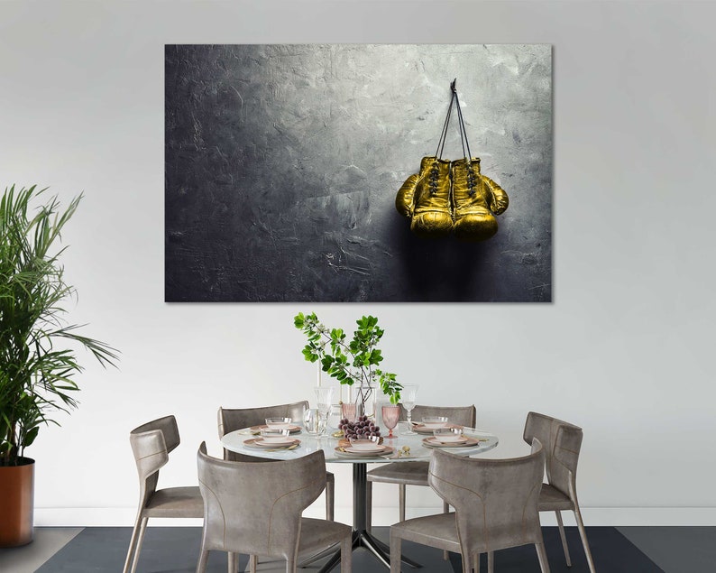 May include: A pair of gold boxing gloves hanging on a hook against a textured gray wall.