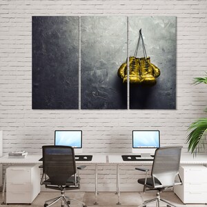 May include: A pair of gold boxing gloves hanging on a dark gray textured wall.