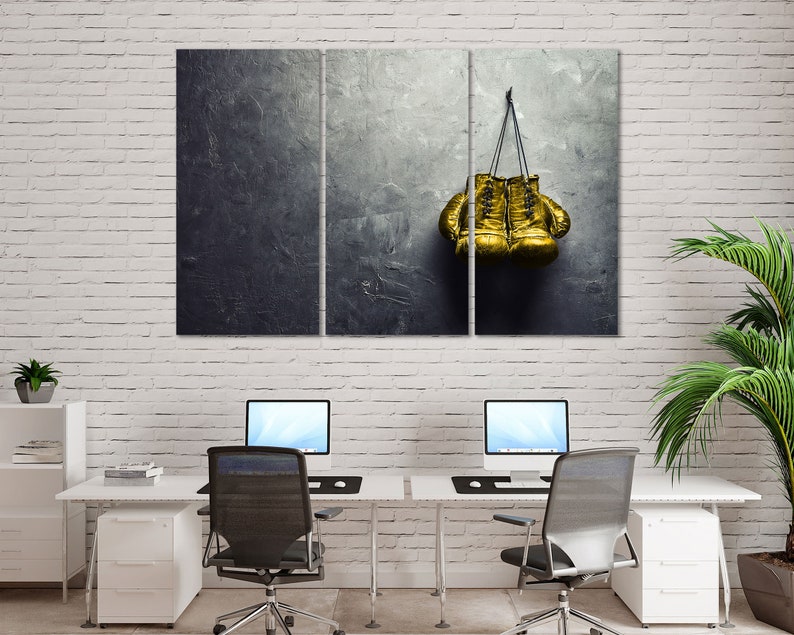 May include: A pair of gold boxing gloves hanging on a dark gray textured wall.