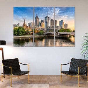 May include: A panoramic view of the Melbourne skyline with modern skyscrapers and a bridge over a river. The city is bathed in warm sunlight, with a blue sky and fluffy clouds.
