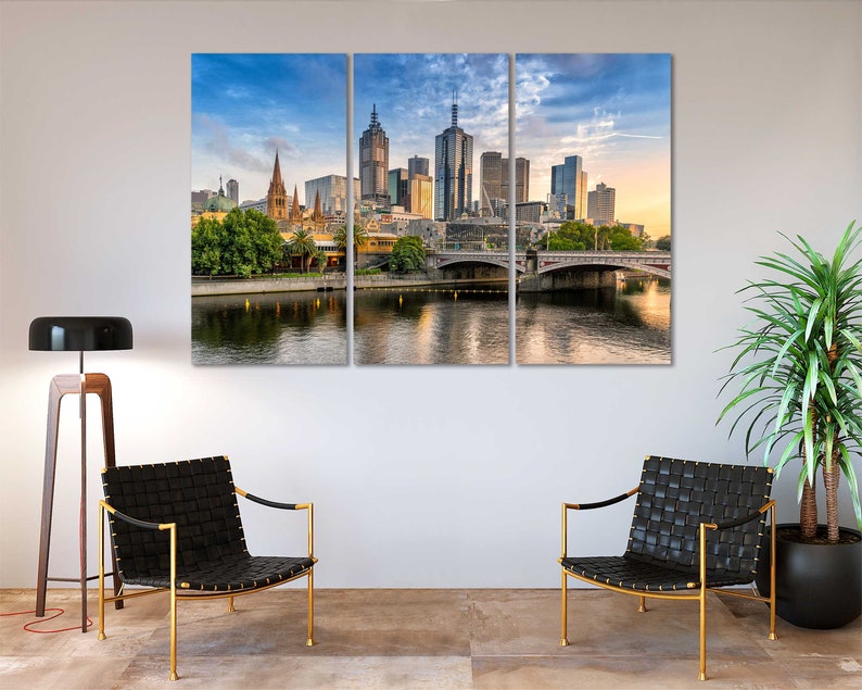 May include: A panoramic view of the Melbourne skyline with modern skyscrapers and a bridge over a river. The city is bathed in warm sunlight, with a blue sky and fluffy clouds.