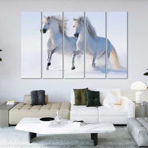 May include: Two white horses run through a snowy field. The horses are running side by side, with their heads turned towards each other. The snow is falling softly around them, creating a peaceful and serene atmosphere.