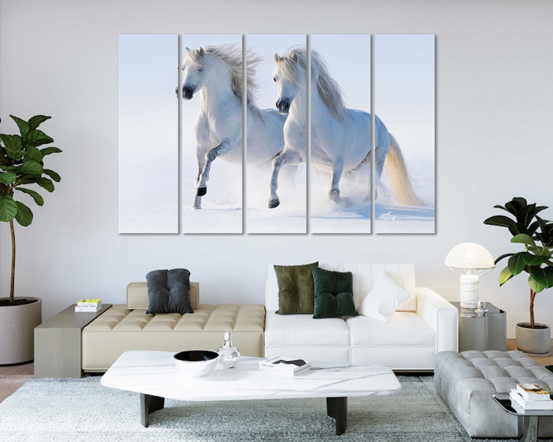 May include: Two white horses run through a snowy field. The horses are running side by side, with their heads turned towards each other. The snow is falling softly around them, creating a peaceful and serene atmosphere.