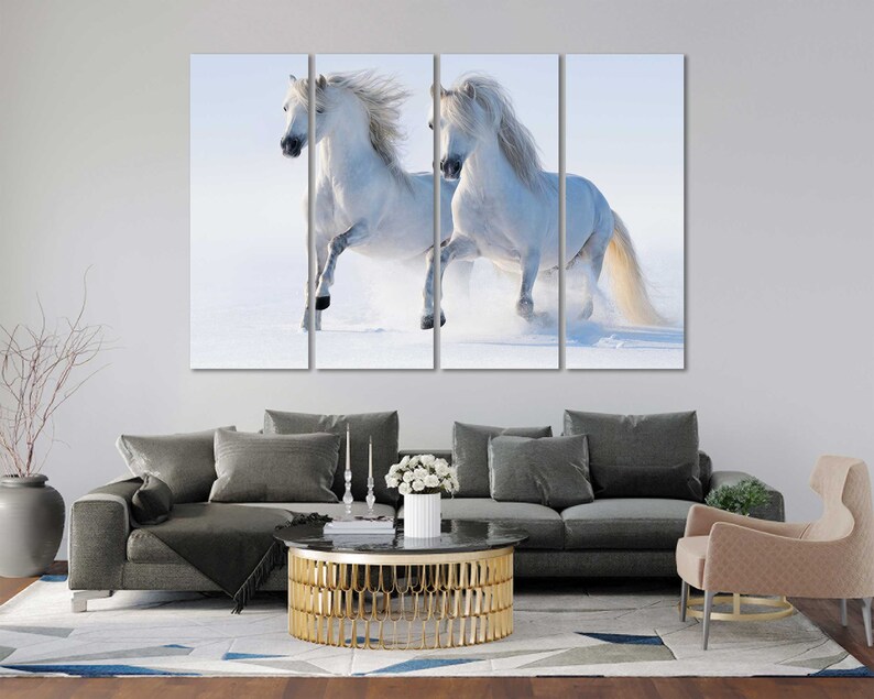 May include: Two white horses run through a snowy field. The horses are running side by side, with their manes flowing in the wind. The snow is falling softly around them, creating a beautiful winter scene.