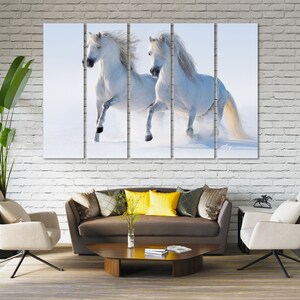 May include: Two white horses running through a snowy field. The horses are running side by side, with their manes flowing in the wind. The snow is flying up around them as they run.