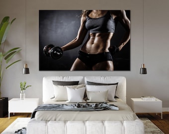 May include: A canvas print with a fitness theme. The image shows a person in athletic wear holding a dumbbell. The person is in a dark setting, with a focus on the physique and the exercise equipment. The print is displayed above a bed.