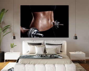 May include: A close-up of a person's torso, glistening with sweat, holding a dumbbell. The person is wearing a black sports bra and black pants. The dumbbell is silver and has a weight of approximately 4.5 kg.
