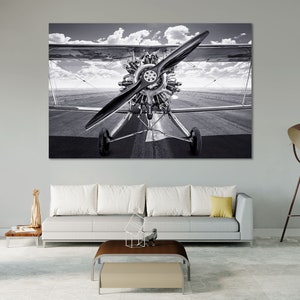 May include: Monochrome image of a classic biplane on a runway. The aircraft has a prominent propeller and radial engine. The sky is filled with clouds, and the plane is centrally positioned in the shot.