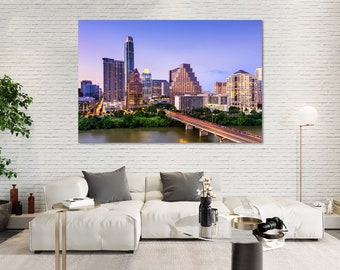 May include: A large canvas print of the Austin, Texas skyline at dusk. The image showcases illuminated skyscrapers, a bridge with car light trails, and a river with green trees. The print is displayed above a white sectional sofa.