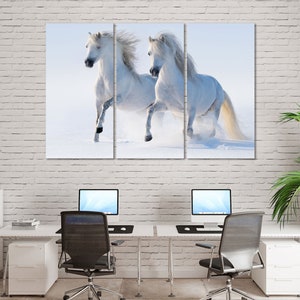 May include: Two white horses running through a snowy field. The horses are running side by side, with their manes flowing in the wind.