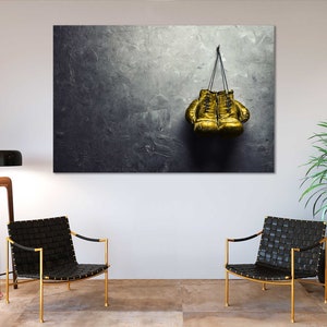 May include: A pair of gold boxing gloves hanging on a hook against a textured gray wall.