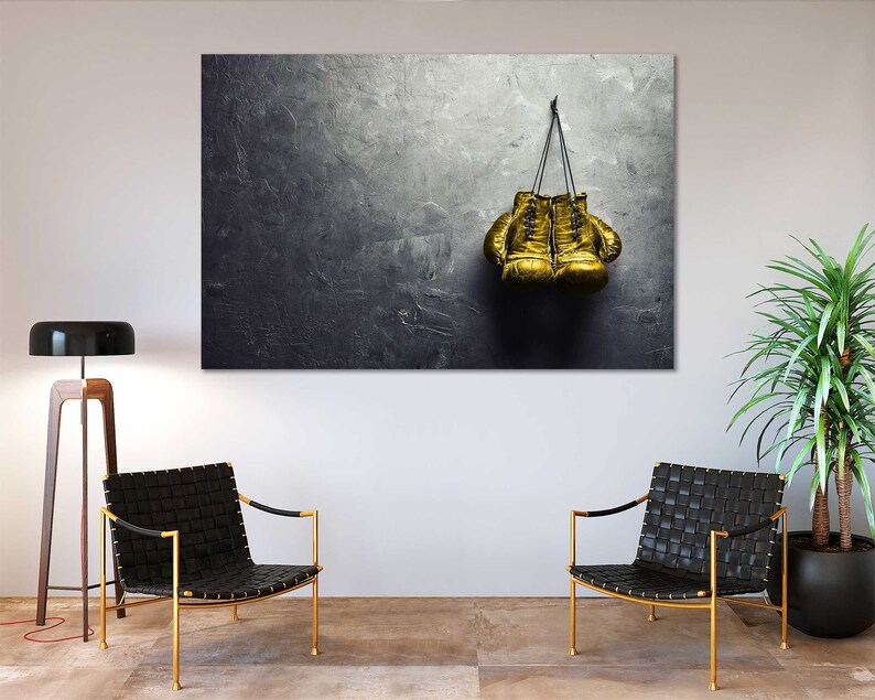 May include: A pair of gold boxing gloves hanging on a hook against a textured gray wall.