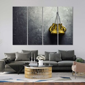 May include: A pair of gold boxing gloves hanging on a hook against a textured gray background.