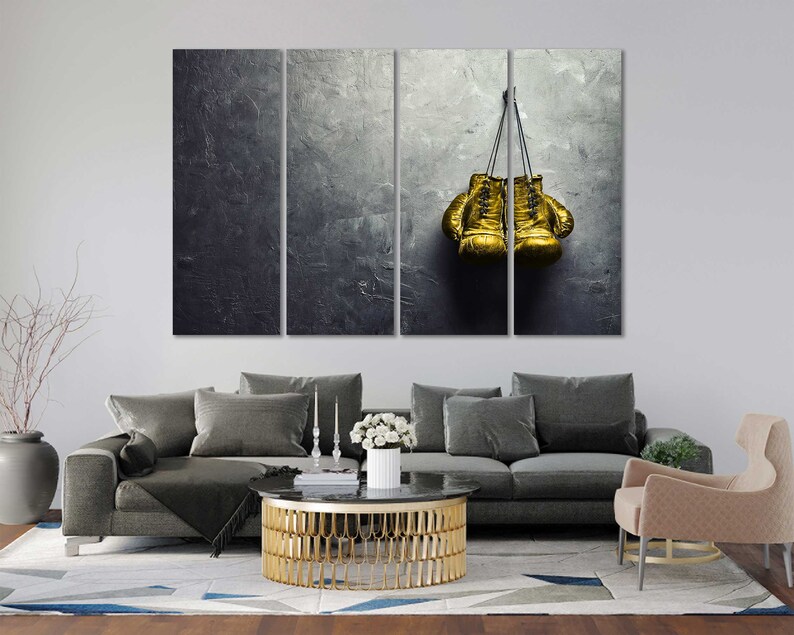 May include: A pair of gold boxing gloves hanging on a hook against a textured gray background.
