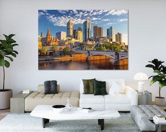 May include: A large canvas print of a cityscape featuring modern skyscrapers and historic buildings. A bridge spans a river in the foreground, reflecting the warm sunlight. The sky is blue with scattered clouds, creating a vibrant and detailed scene.
