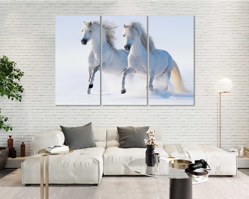 May include: Two white horses run through a snowy field. The horses are running side by side, with their manes flowing in the wind.