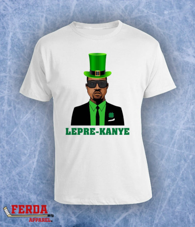 K&ouml;nnte beinhalten: Wei&szlig;es T-Shirt mit einer Cartoon-Abbildung eines Mannes in einem gr&uuml;nen Leprechaun-Hut, Sonnenbrille und Anzug. Der Text "LEPRE-KANYE" ist unter dem Bild gedruckt.