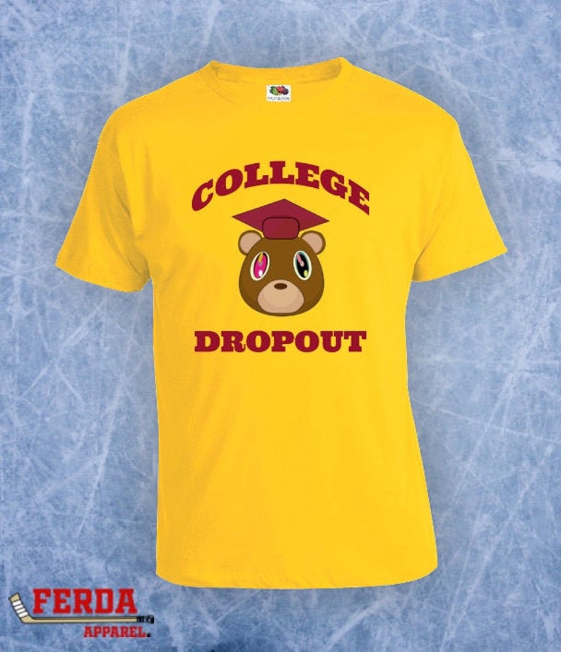 Pode incluir: Camiseta amarela com um urso de desenho animado vermelho e marrom usando um chap&eacute;u de formatura. O texto "COLLEGE DROPOUT" est&aacute; impresso na camiseta.