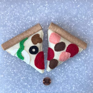 May include: Two felt pizza slices with beige crusts and various toppings. One slice has green, white, black, and brown toppings. The other has red, pink, and brown toppings. A penny is next to the pizza slices.