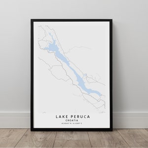 May include: A black framed print of a map of Lake Peruca in Croatia. The lake is outlined in blue and the surrounding area is shown in gray. The text "LAKE PERUCA CROATIA 43.8260° N, 16.5380° E" is printed below the map.