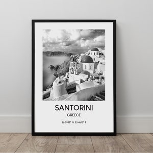 Puede incluir: Una fotograf&iacute;a en blanco y negro de Santorini, Grecia. La imagen muestra un pueblo encalado con iglesias de c&uacute;pulas azules, con vistas al mar Egeo. El texto "SANTORINI GRECIA 36.3932&deg; N, 25.4615&deg; E" est&aacute; impreso debajo de la imagen.