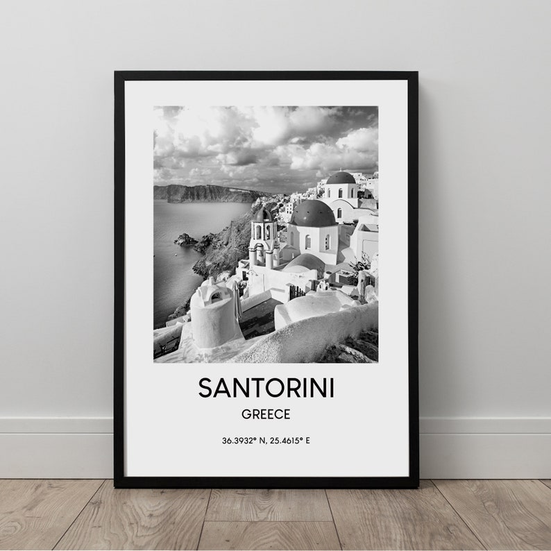 Puede incluir: Una fotograf&iacute;a en blanco y negro de Santorini, Grecia. La imagen muestra un pueblo encalado con iglesias de c&uacute;pulas azules, con vistas al mar Egeo. El texto "SANTORINI GRECIA 36.3932&deg; N, 25.4615&deg; E" est&aacute; impreso debajo de la imagen.