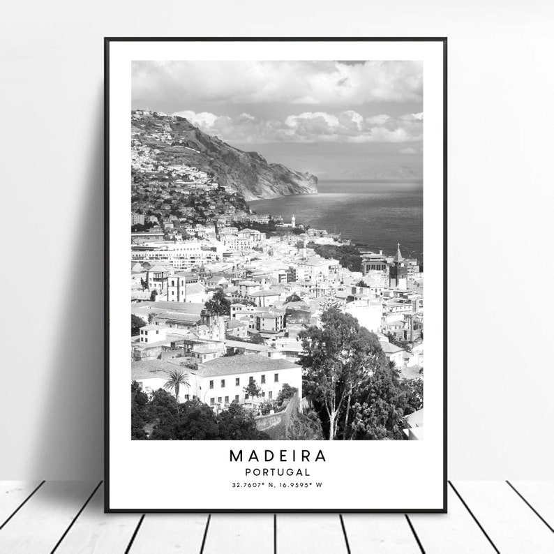 Op de afbeelding: Een zwart-witfoto van een kuststad met een berg op de achtergrond. De tekst "MADEIRA PORTUGAL 32.7607&deg; N, 16.9595&deg; W" staat onderaan de afbeelding.