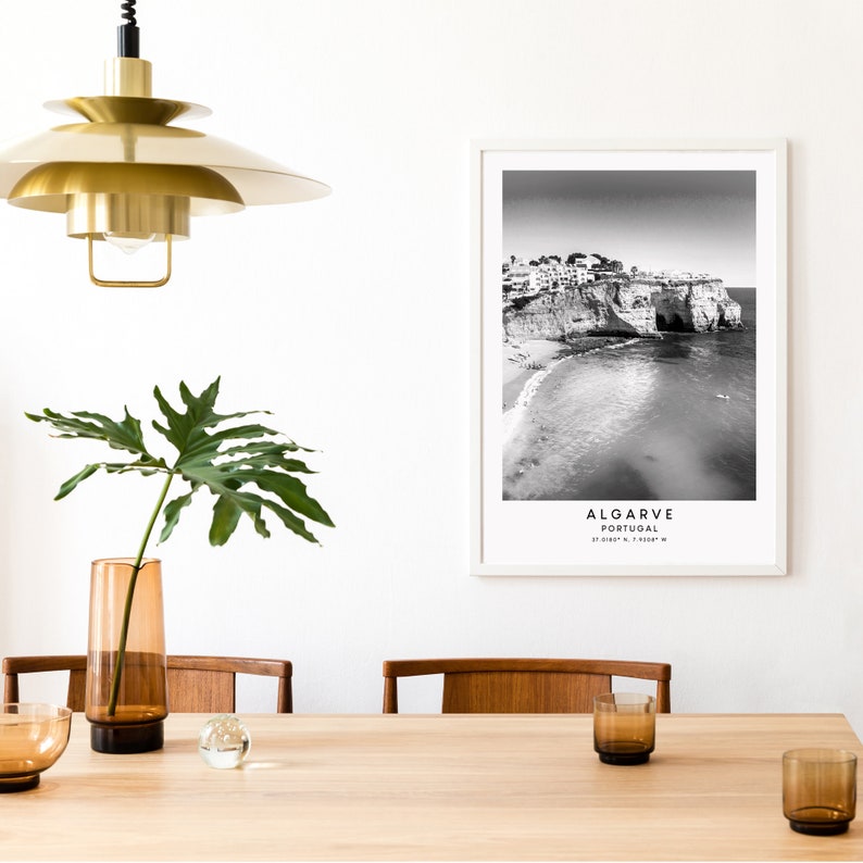 May include: Black and white photograph of a beach in Algarve, Portugal. The photo shows a rocky cliff with buildings on top, a sandy beach, and the ocean. The text "ALGARVE PORTUGAL 37.0188&deg; N, 7.9308&deg; W" is printed below the image.