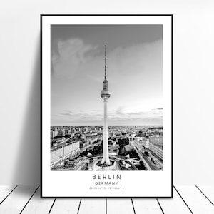 May include: Black and white photograph of the Berlin skyline featuring the iconic Fernsehturm tower in the centre. The text "BERLIN GERMANY 52.5200° N, 13.4050° E" is at the bottom of the image.