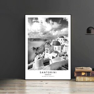 Puede incluir: Fotograf&iacute;a en blanco y negro de Santorini, Grecia. La imagen muestra edificios blancos con c&uacute;pulas azules, una costa rocosa y una masa de agua. El texto "SANTORINI GREECE 36.3932&deg; N, 25.4615&deg; E" est&aacute; impreso en la parte inferior de la imagen.