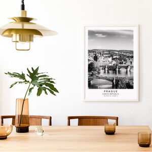 May include: Black and white photograph of Prague, Czech Republic, with the text "Prague, Czech Republic" and coordinates below. The photo shows a cityscape with a river and bridges.