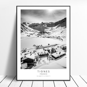 Könnte beinhalten: Schwarzweißfoto eines verschneiten Bergdorfes mit einem zugefrorenen See im Vordergrund. Der Text "Tignes France 45.4683° N, 6.9056° E" befindet sich am unteren Rand des Bildes.