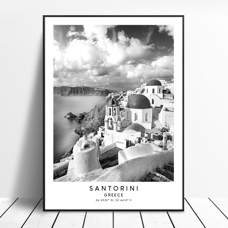 Puede incluir: Fotograf&iacute;a en blanco y negro de Santorini, Grecia. La imagen muestra edificios blancos con techos abovedados azules, una iglesia y una vista del mar Egeo. El texto "SANTORINI GREECE 36.3932&deg; N, 25.4615&deg; E" est&aacute; en la parte inferior de la imagen.