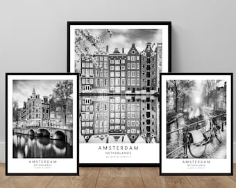 May include: Three framed black and white prints of Amsterdam scenes. The prints feature iconic canals, bridges, and buildings. Each print has the word "AMSTERDAM" and coordinates at the bottom. The largest print shows a reflection of buildings in the water.