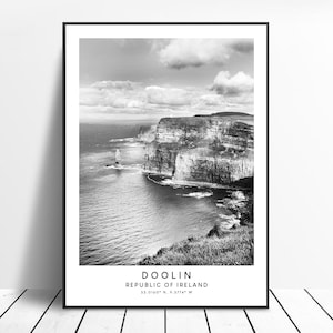 May include: Black and white photograph of the Cliffs of Moher in Doolin, Republic of Ireland. The image shows the dramatic cliffs rising from the sea, with a view of the coastline and the ocean.