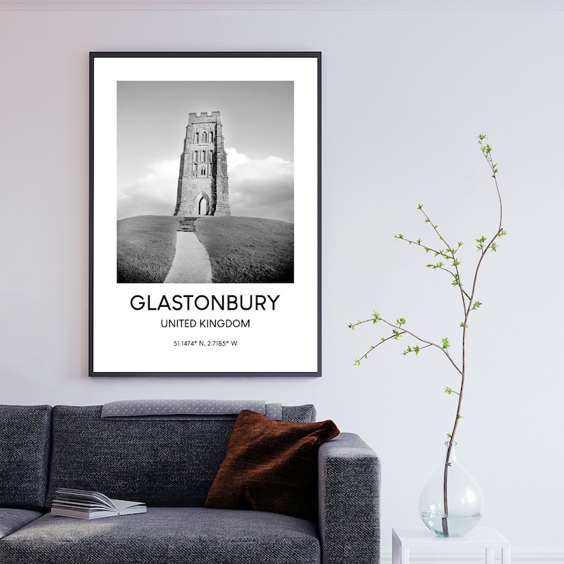 May include: Black and white photograph of Glastonbury Tor, a historic tower in Glastonbury, United Kingdom. The image features a stone tower on a grassy hill with a path leading up to it. The text "Glastonbury, United Kingdom, 51.1424&deg; N, 2.7185&deg; W" is printed below the image.