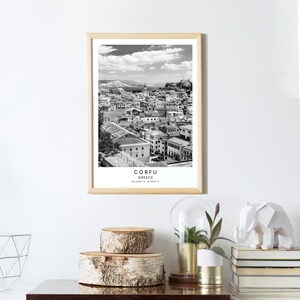 May include: Black and white photograph of the city of Corfu, Greece. The photo shows a cityscape with buildings and a cloudy sky. The text "CORFU GREECE 39.6147&deg; N, 19.9019&deg; E" is printed below the image.