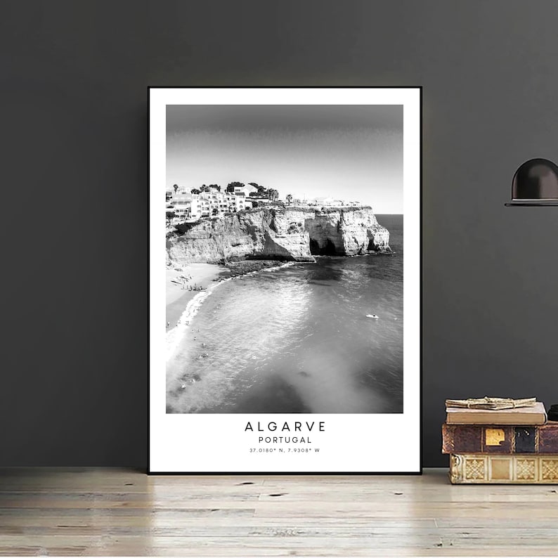 May include: Black and white photograph of a rocky coastline with a beach and buildings in the distance. The text "ALGARVE PORTUGAL 37.0180&deg; N, 7.9208&deg; W" is printed below the image.