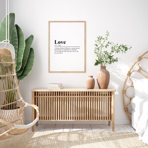 May include: A framed print with a white background and black text that reads "Love" and its definition. The print is hanging on a white wall in a room with a wooden cabinet, a hanging chair, and a bed with a white headboard.