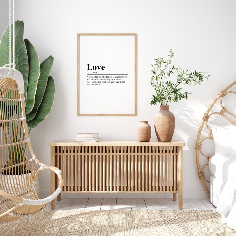 May include: A framed print with a white background and black text that reads "Love" and its definition. The print is hanging on a white wall in a room with a wooden cabinet, a hanging chair, and a bed with a white headboard.