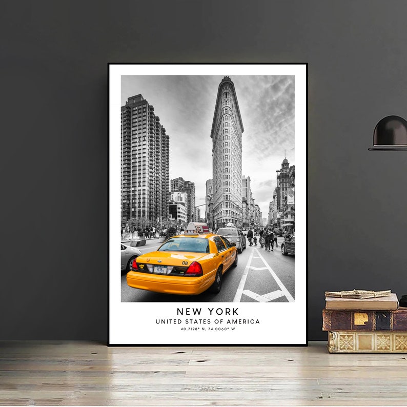 May include: A black and white photograph of a yellow taxi cab driving down a street in New York City. The Flatiron Building is in the background. The text "NEW YORK, UNITED STATES OF AMERICA, 40.7128&deg; N, 74.0060&deg; W" is at the bottom of the image.