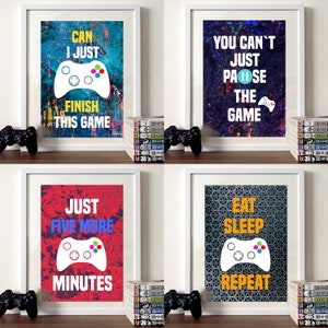 Pode incluir: Quatro impressões emolduradas com texto temático de jogos e um controlador de videogame estilizado. As impressões têm um fundo colorido e abstrato. O texto nas impressões diz: "Can I just finish this game", "You can't just pause the game", "Just five more minutes", e "Eat sleep repeat".