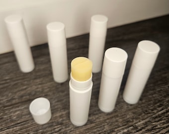 May include: A close-up of six white lip balm tubes, one of which has a yellow lip balm stick inside. The tubes are on a wooden surface.