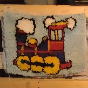 May include: A blue and white rug with a colorful train design. The train is red, yellow, black, and blue. The train has two smoke stacks and two wheels.