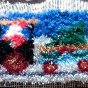 May include: A colorful rug depicting a train with three cars, each decorated with a Christmas tree and red and green accents. The train is on a white background with blue and white fluffy yarn.