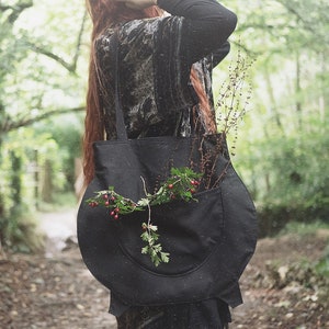 Peut inclure: Un sac fourre-tout noir avec une grande poche sur le devant. Le sac est rempli de brindilles de verdure et de baies rouges.